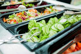 Frisches Salatbuffet mit Gurkenscheiben, gemischtem Blattsalat und Gemüse in Edelstahlbehältern
